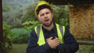 Kırsal kesimdeki taş binanın yanında sarı kasketli ve çelik yelek giyen genç inşaat işçisi, acılı acil durum..