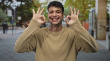 Erkek, açık havada güneş ışığında iyi bir sembol oluşturmak için ellerini kaldırır. İspanyol adam, açık bir şekilde onaylamak için sevinçle gülümsüyor..