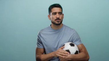 İzole edilmiş mavi duvarın önünde futbol topu tutan genç İspanyol bir adam ciddi ile derin düşüncelere dalmış, yakışıklı özelliklerini sergiliyor..