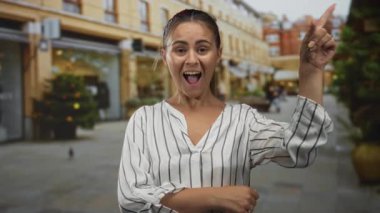 Dükkanların yanındaki sokakta parmaklarını yukarı doğru gösteren İspanyol kadın ağzı açık gülümsüyor ve el hareketi yapıyor; sevinç kutlaması.
