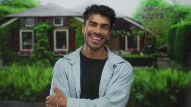 Açık havada yeşil yeşilliklerin arasında tuğla bina girişinin yanında kolları çapraz duran İspanyol genç adam, güven..