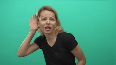Siyah gömlek giyen genç sarışın kadın yeşil stüdyo ortamında el pençe divan duruyor..