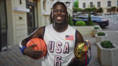 Basketbol ve altın kupa tutan adam, Amerika 'da kaldırım taşı bir sokakta gülümsüyor..