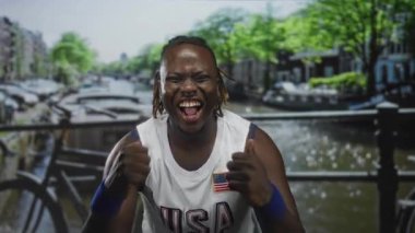 Amerika forması ve bileklikleriyle sokakta yumruk atan ve gülen bir adam. Heyecan verici bir zafer..