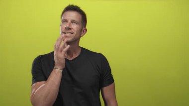 Eli çenesinde ve parmakları kireç yeşili stüdyoda yukarı bakan siyah tişört ve bilezik giyen düşünceli iyimser bir adam..