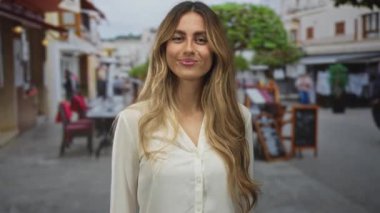 Beyaz bluzlu sarışın kadın, kaldırım taşı sokağındaki kalabalık bir kafede parmak ucuyla tapınağı işaret ediyor..