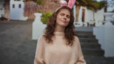 Tavşan kulaklı bir kadın şehir sokaklarında gün ışığında rahat bir kazakla neşeli şehir hayatının özünü neşeli bir ifadeyle yakalıyor..