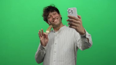 Hispanik bir adam dondurma ile selfie çekerken gülümsüyor canlı yeşil bir arka plana karşı, oyuncu bir unsur ekleyerek.