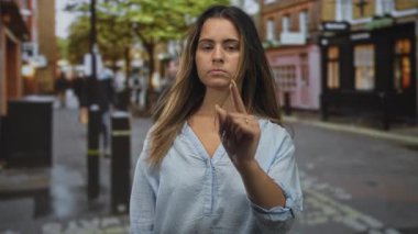 Islak bir şehir caddesindeki kamerayı gösteren kadın parmağı. Cübbeler, mağazalar ve yakınlarda yürüyen bulanık yayalar. Kararlılık..