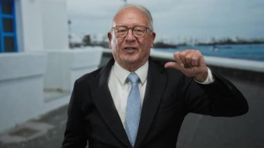 Takım elbiseli kıdemli adam, sokak ortamında başparmaklarıyla güvenle el kol hareketi yapıyor, canlı şehir ortamında iş cazibesini kucaklıyor..