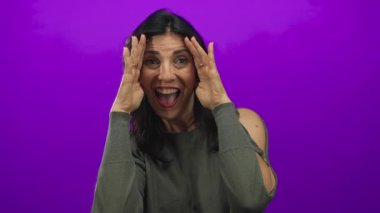 Orta yaşlı İspanyol kadın gülümserken mor bir stüdyoda elleri ile yüzünü örtüyor ve açıyor. Mutluluk..