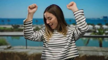 Deniz kenarında çizgili tişört giyen bir kadın güneşli bir günde açık havada, canlı limanda, deniz manzaralı ve palmiye ağaçlarıyla okyanus teknesinin yanında duruyor..