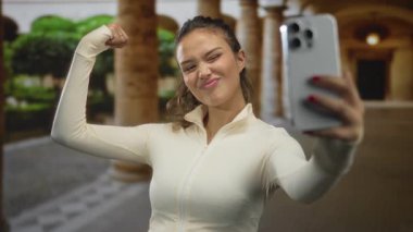 Taş kolları olan bir avluda akıllı telefonla kollarını esneten İspanyol genç bir kadın. Güç motivasyonu güveni arttırıyor..