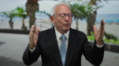 Kıdemli bir adam, deniz kenarında bir gezinti alanında hareketli hareketler yapıyor, canlı ve profesyonel bir açık hava sahnesi yakalıyor palmiye ağaçları ve okyanus manzaralı..