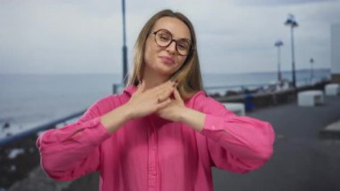 Pembe gömlekli kadın kumsalda gezinirken gülümsüyor kolları ardına kadar açık, dışarıda neşe ve huzuru yakalıyor..