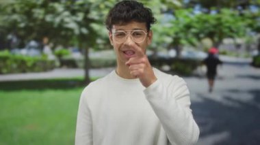 Parlak gün ışığı altında, arkasında bulanık ağaçlar olan yemyeşil parktaki kamerayı gösteren adam kendine güveni savunuyor..