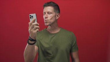 Akıllı telefon tutan, konuşan ve kırmızı stüdyoda el sallayan adam yeşil tişört giyiyor; dostça bağlantı sanal sohbet.
