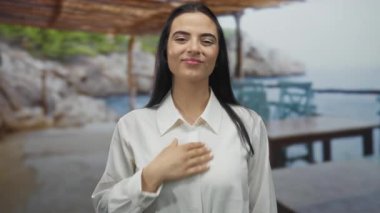 Deniz kenarındaki bulanık arka planda gülümseyen bir kadın güneşli bir günde sakin ve barışçıl bir tavır sergiliyor..