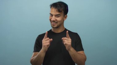 Genç adam gülümsüyor ve canlı mavi bir arka plana bakıyor. İzole edilmiş bir stüdyoda kendinden emin ve dostane bir enerji taşıyor.
