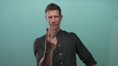 Stüdyoda elleri öne doğru uzanan siyah gömlekli ve mavi duvarlı görünür bilezik takan bir adam..