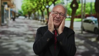Takım elbiseli kıdemli bir adam ağaçlarla kaplı bir sokakta neşeli bir şekilde gülümsüyor. Mutluluğu ve şehir ortamında başarılı bir emekliliği iletiyor..