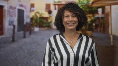 Kadın gülümsüyor ve el hareketleriyle güneş ışığıyla aydınlanan kaldırım taşı caddesinde tarihi yapı cepheleriyle; mutluluk.