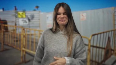 Şantiyedeki gülümseyen, sıradan bir süveter giyen, çitlerle ve tabelalarla çevrili genç İspanyol kadın açık hava kentsel bir ortam öneriyor..