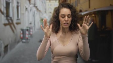 Elleri havada bir kadın dar bir kaldırım taşı şehir sokak sokak üzerinde, pembe uzun kollu gömlek ve yüzükler giymiş, ileriye bakıyor; sürpriz.