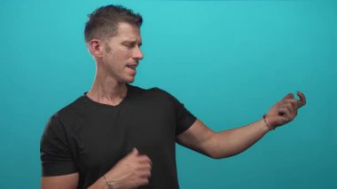 Kafkasyalı genç adam, turkuaz bir stüdyoda kapalı gözlerle şarkı söylerken sağ elini işaret ediyor ve el kol hareketi yapıyor..