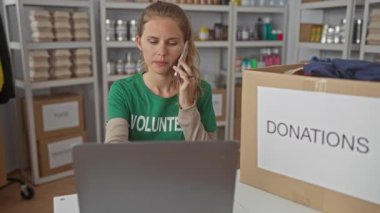 Kadın, depodan ararken telefonu tutuyor, dizüstü bilgisayarda yazıyor gönüllü olarak bir kutunun yanındaki rafta bağış organize ediyor ve envanterleri kontrol ediyor..