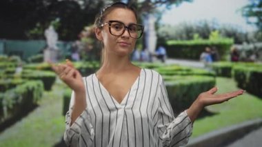 Kadın, çitleri ve heykeli olan yeşil bir parkta avucunun içini işaret ediyor..