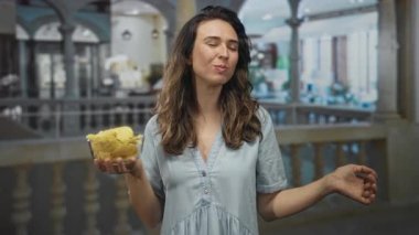 Kadın otel lobisinde yüzüne yakın cipsleri kokluyor. Gözleri kapalı ve el hareketleriyle havalara uçuyor..