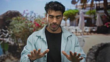Avuç içleri açık renk kot gömlek giyen İspanyol genç adam gün ışığı altında teras inşaatında yatıştırıcı bir jest olarak yükseltildi..