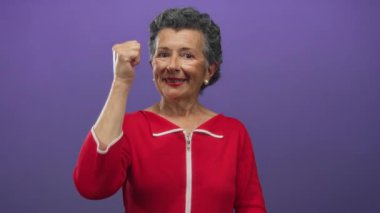 Kırmızı elbiseli son sınıf öğrencisi kadın canlı mor bir arka plana karşı olumlu bir jest sergiliyor. Kendine güveni ve neşesi yüksek..