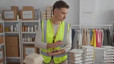 Yansıtıcı yelek giyen genç adam bağış kutuları ve yiyecek paketleriyle çevrili bir hayır kurumunda gönüllü olarak çalışıyor..