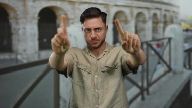 Sakallı genç adam, parmakları Roma Kolezyumu 'nda açık havada, günlük gömlek giyiyor, tarihi mimariye karşı beyaz yüz hatları sergiliyor..