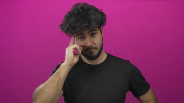 Sakallı genç İspanyol bir adam canlı pembe bir arka plana karşı düşünceli ve odaklanmış görünüyor..