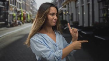 Kadın, şehrin kaldırım taşı sokağında sağı işaret ediyor, mavi gömlek ve sarı tırnaklar görünür; kendine güvenen kentsel.