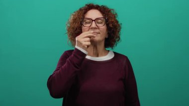 Kıvırcık esmer saçlı bir kadın yeşil bir duvara öpücük yolluyor. Arka plan izole edilmiş, gözlüklü ve bordo bir kazak giyiyor. Dostça ve sıcak bir atmosferi çağrıştırıyor..