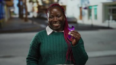 Mor kurdeleli bir kadın, şehir sokaklarında yeşil süveter içinde farkındalık ve toplum desteğini kutluyor..