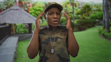 Kamuflaj üniformalı genç Afrikalı Amerikalı kadın elinde künyeyle ormanda iki elini de kaldırdı..