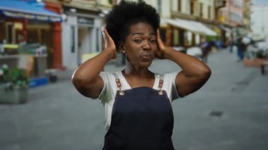Önlüklü Afro-Amerikalı genç bir kadın kalabalık bir şehir caddesinde duruyor, açık bir şehir ortamının ortasında neşe ve güveni ifade ediyor..