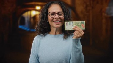 Bir şehir caddesinde elinde Arjantin pezosu tutarken gülümseyen bir kadın, canlı bir fon ile finansal temalar sergiliyor..