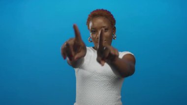 Beyaz tişörtlü, gülümseyen ve kamerayı stüdyoya çeviren genç Afro-Amerikan kadın..