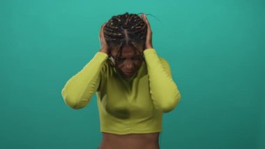 El ele tutuşup kulaklarını kapatan balıkçı yaka giyen kadın deniz mavisi bir stüdyoda göbek bağını ortaya çıkarıyor..