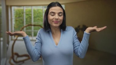 Latin kökenli genç bir kadın oturma odasında duruyor. Rahatlamış bir evde kayıtsızlık ve şaşkınlık ifadesi sergiliyor..