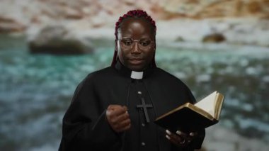 Din adamları gibi giyinmiş bir kadın deniz kenarında kitap okuyup el kol hareketleri yapıyor. Doğal arka planı olan sakin bir ortamda inanç ve maneviyatı sembolize ediyor..