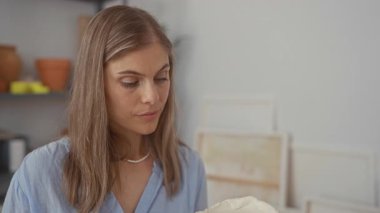 Kadın, güneş ışığıyla aydınlanan sanatsal atölyede dikkatle bakan el yapımı kilden bir form tutuyor; konsantrasyon..