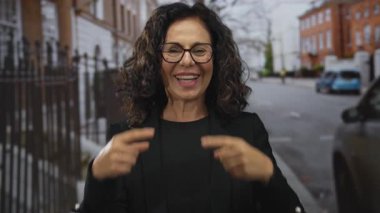 Orta yaşlı İspanyol kadın şehir sokaklarında sessizlik için parmaklarını işaret ediyor; sessiz, şakacı gizlilik.