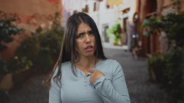 Genç bir kadın gün ışığında dar bir sokakta kendini işaret ediyor; reddedilme..